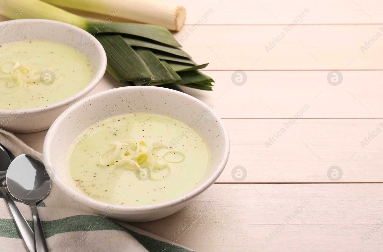 Photo of Bowls of tasty leek soup on white wooden table. Space for text