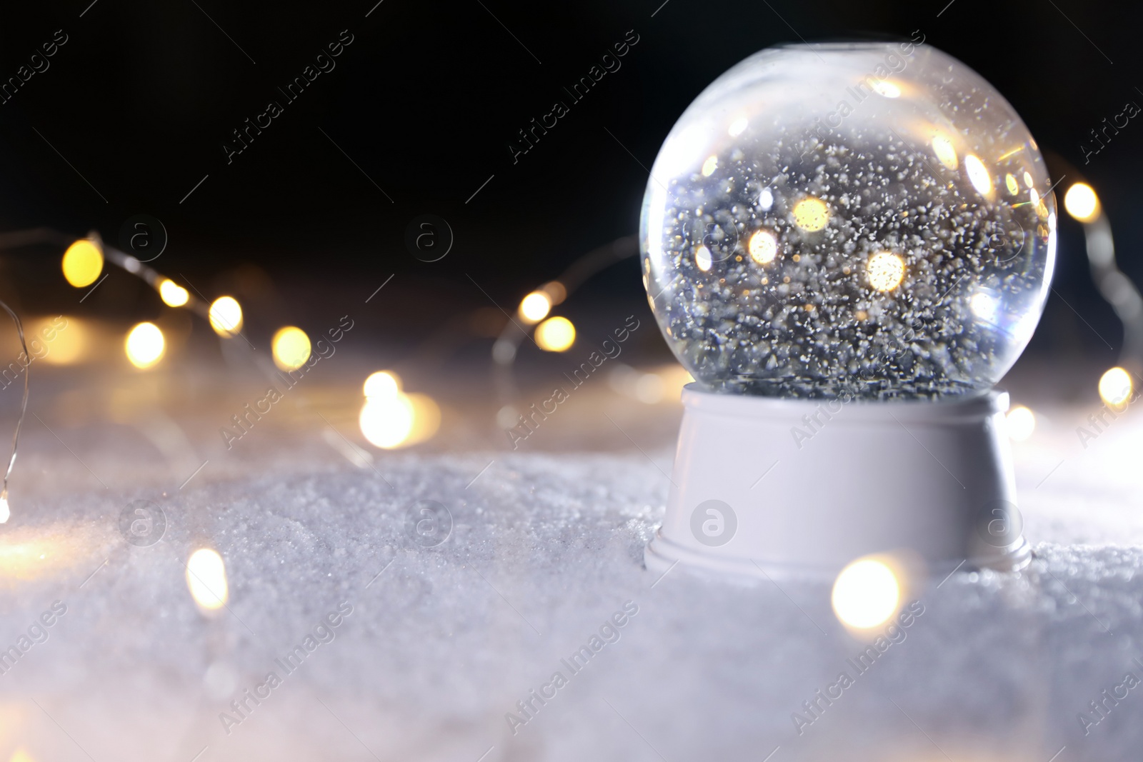 Photo of Crystal globe and Christmas lights on white snow outdoors. Space for text