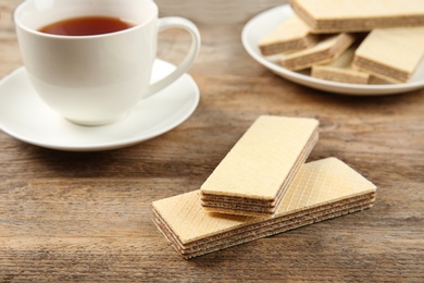 Delicious wafers with cup of tea on brown wooden background