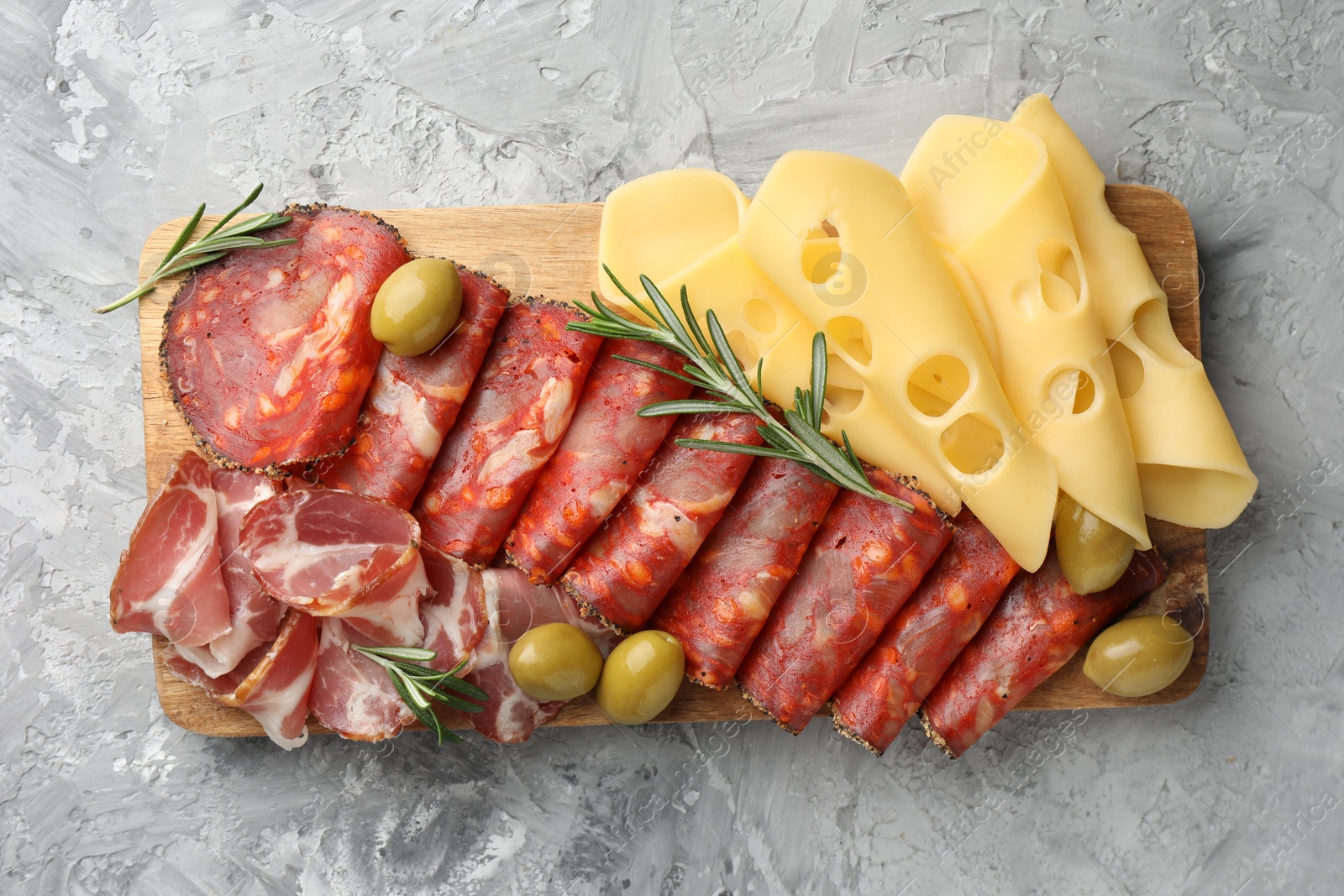 Photo of Charcuterie board. Delicious cured ham, cheese, sausage, olives and rosemary on light grey table, top view