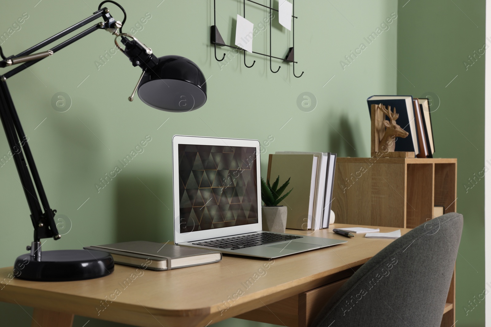 Photo of Modern laptop, books, lamp and stationery on wooden desk near green wall. Home office