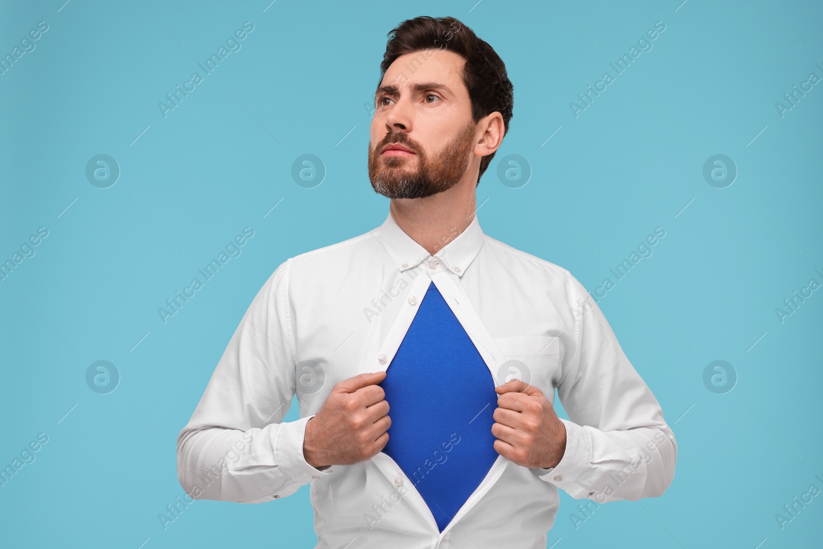 Photo of Confident businessman wearing superhero costume under suit on light blue background