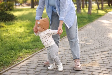 Photo of Mother supporting her baby while he learning to walk outdoors, closeup