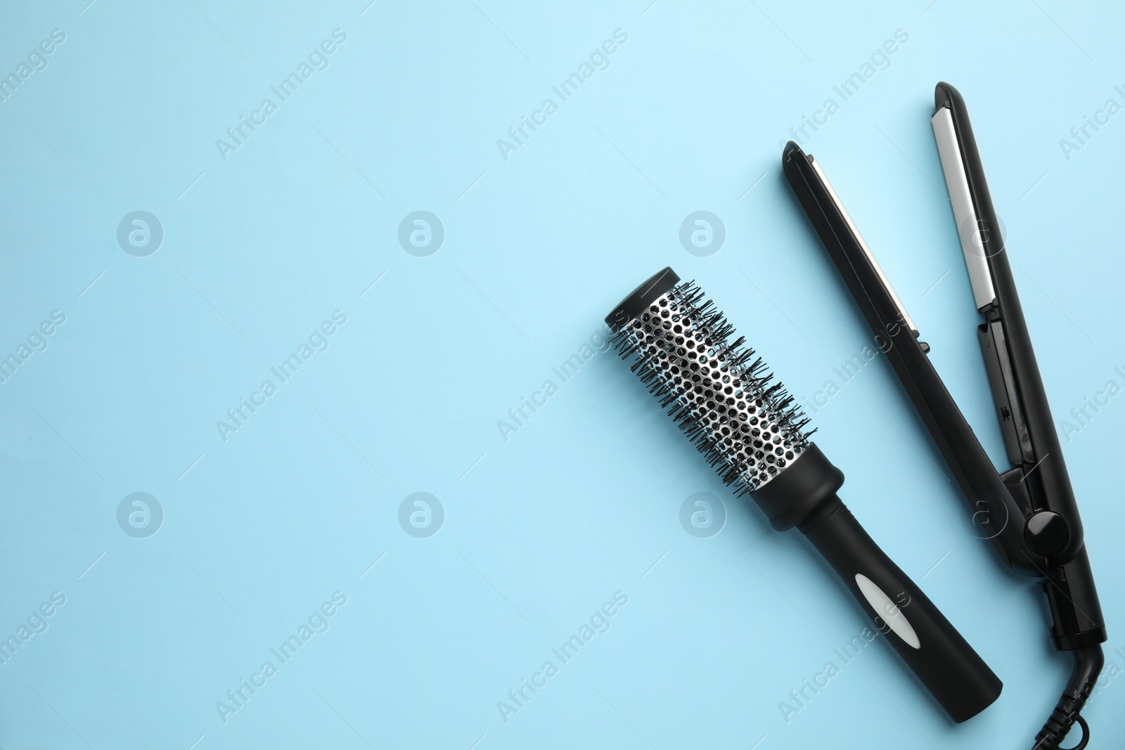 Photo of Hair straightener and round brush on light blue background, flat lay. Space for text