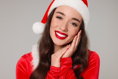 Photo of Christmas celebration. Beautiful young woman in Santa hat on grey background