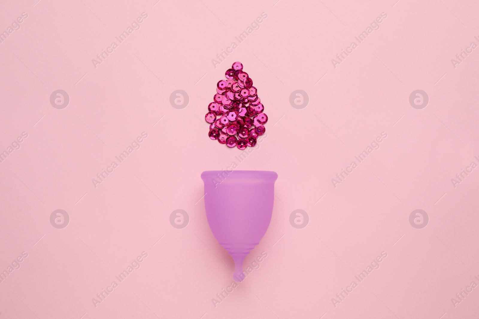 Photo of Menstrual cup near drop made of sequins on pink background, flat lay