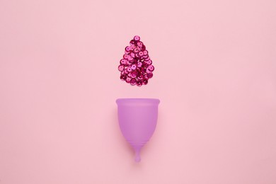 Menstrual cup near drop made of sequins on pink background, flat lay