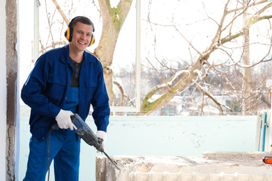 Worker using rotary drill hammer for window installation indoors