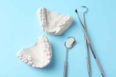 Dental model with gums and dentist tools on light blue background, flat lay. Cast of teeth