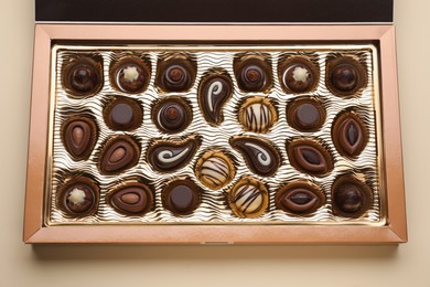 Box of delicious chocolate candies on beige background, top view