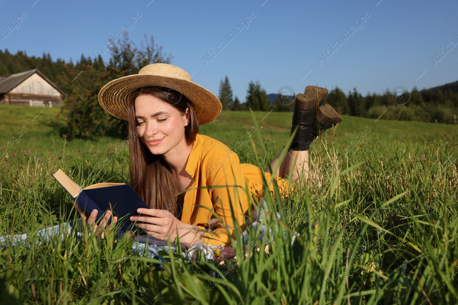 Photo of Beautiful young woman reading book on green meadow