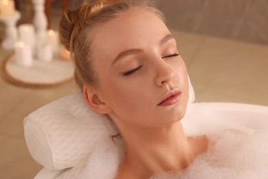 Photo of Young woman using pillow while enjoying bubble bath indoors