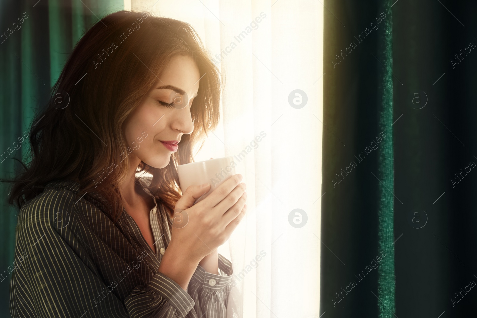Image of Woman drinking coffee near window with beautiful curtains at home