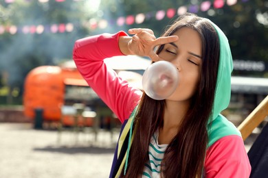 Beautiful young woman blowing chewing gum and showing peace gesture outdoors