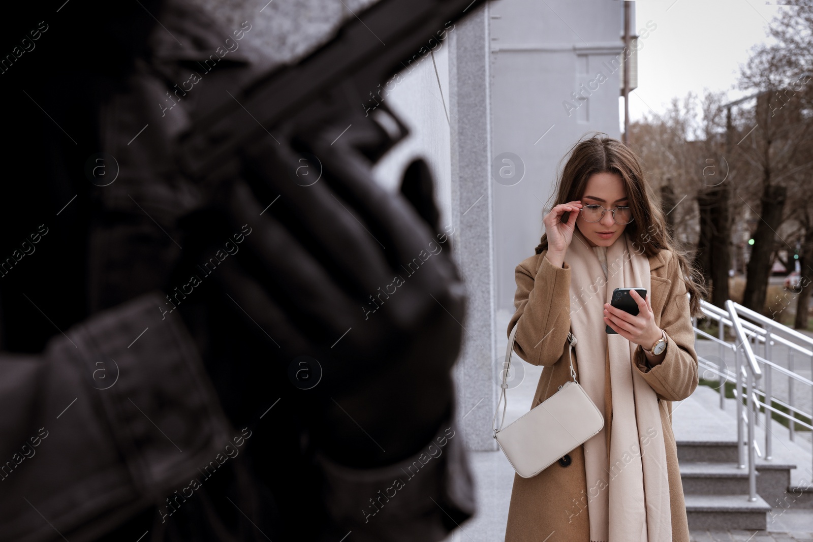 Photo of Criminal with gun hiding behind wall and waiting for woman on city street