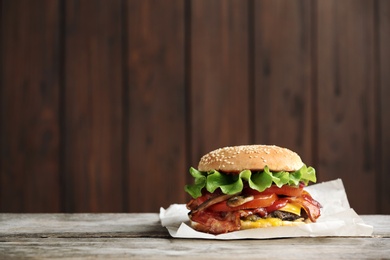 Photo of Tasty burger with bacon on wooden table. Space for text