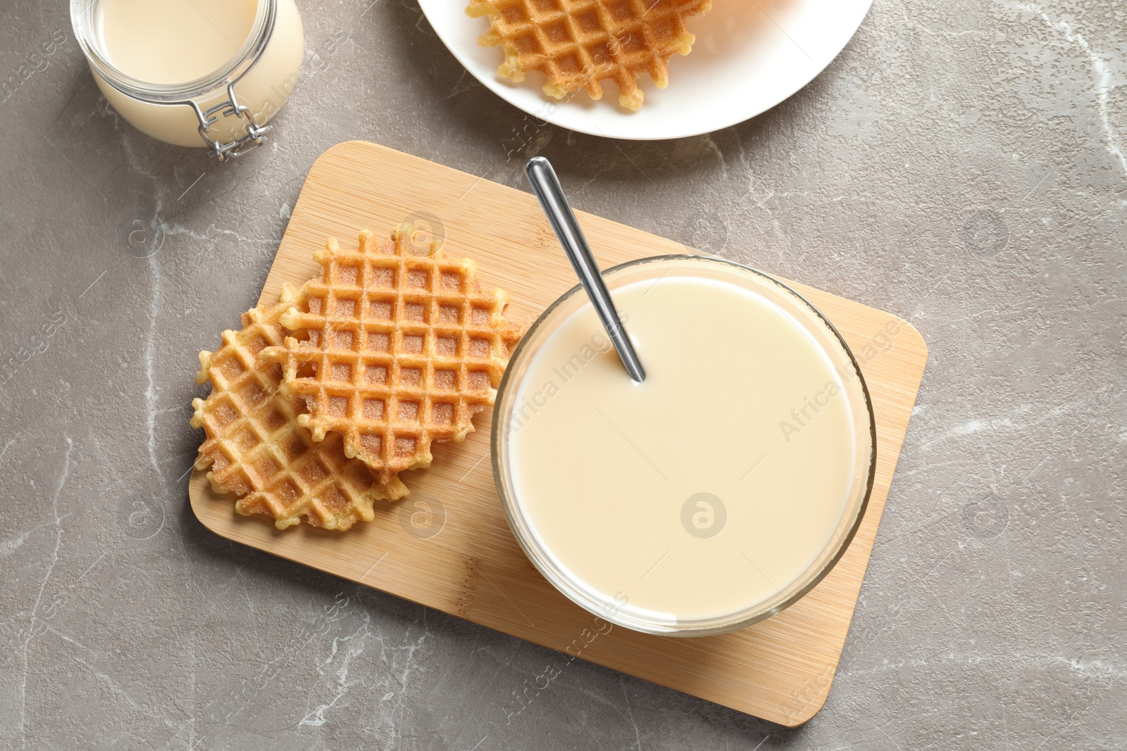 Photo of Bowl of condensed milk and waffles served on grey table, top view. Dairy products