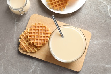 Bowl of condensed milk and waffles served on grey table, top view. Dairy products