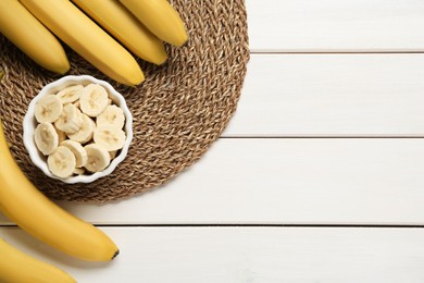 Photo of Bowl with cut bananas near whole fruits on white wooden table, flat lay. Space for text