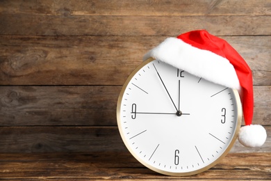 Clock with Santa hat showing five minutes until midnight on wooden background, space for text. New Year countdown