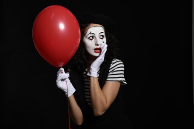 Photo of Young woman in mime costume with balloon posing on black background