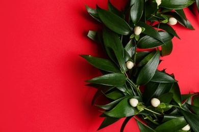 Photo of Beautiful handmade mistletoe wreath on red background, top view. Space for text