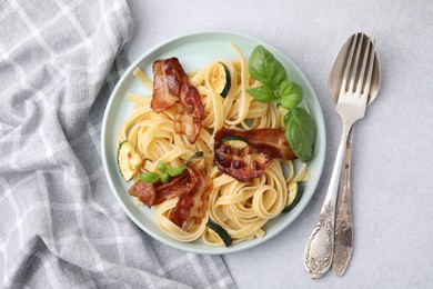 Photo of Tasty pasta with bacon and cutlery on light grey table, top view