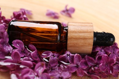 Bottle with essential oil and lilac flowers on wooden surface, closeup