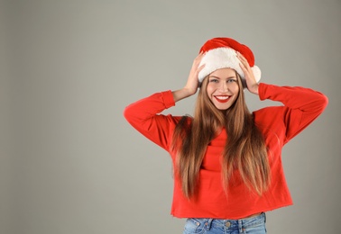 Young beautiful woman in Santa hat on grey background. Christmas celebration