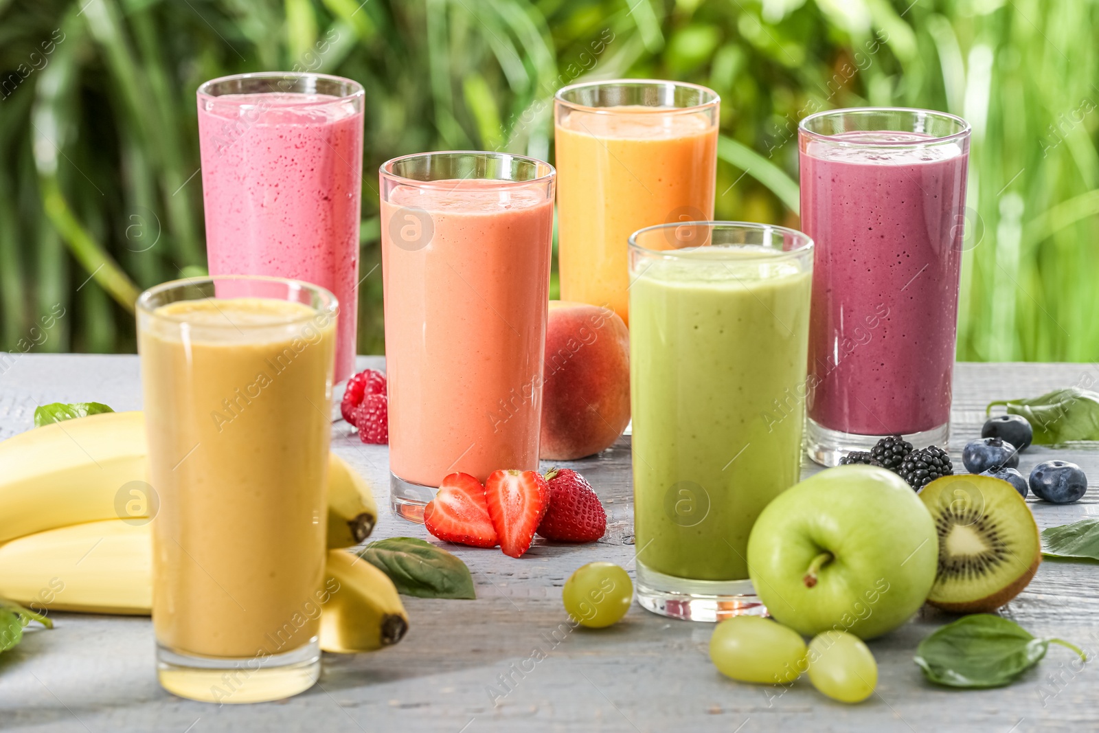 Photo of Many different delicious smoothies and ingredients on grey wooden table against blurred background