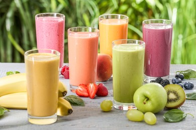 Photo of Many different delicious smoothies and ingredients on grey wooden table against blurred background
