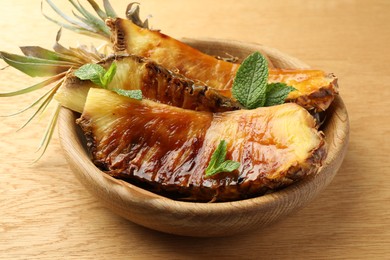 Tasty grilled pineapples in bowl on wooden table, closeup