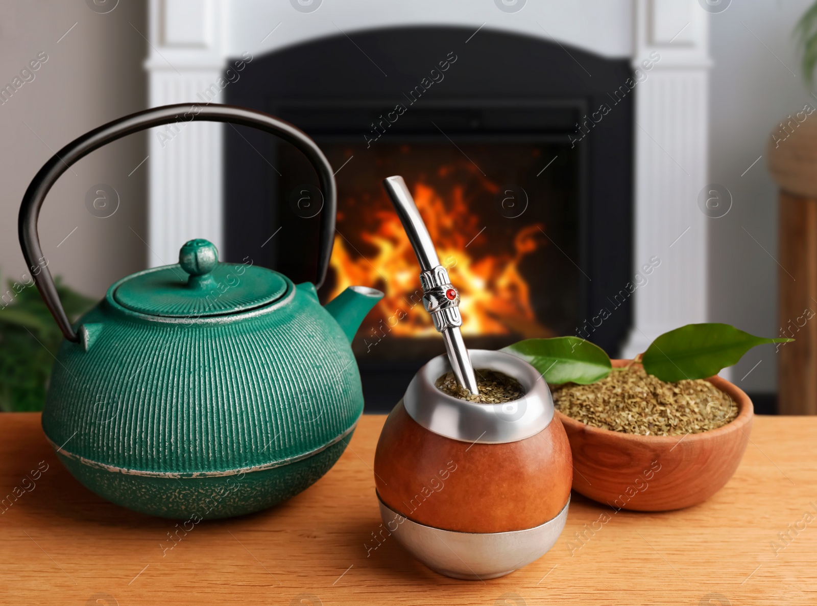 Image of Calabash with mate tea, bombilla and teapot on wooden table near fireplace