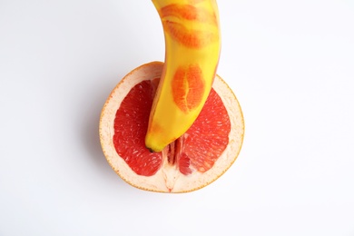 Fresh grapefruit and banana with red lipstick marks on white background, top view. Sex concept