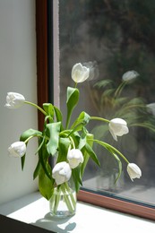 Photo of Bouquet of beautiful white tulip flowers in glass vase on windowsill indoors