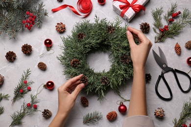 Photo of Florist making beautiful Christmas wreath with pine cones at grey table, top view