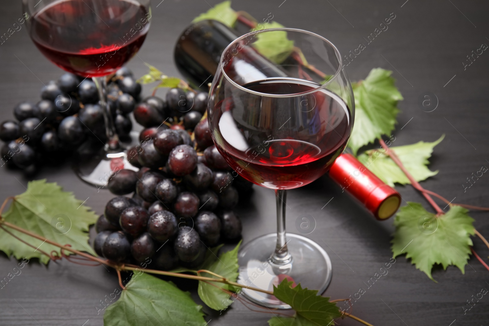 Photo of Glass and bottle of red wine and fresh ripe juicy grapes on table