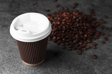Coffee to go. Paper cup and roasted beans on grey table, closeup. Space for text