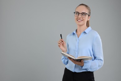 Happy young secretary with notebook and pen on grey background, space for text