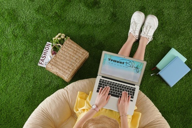 Woman holding laptop with open travel blogger site on artificial grass, top view
