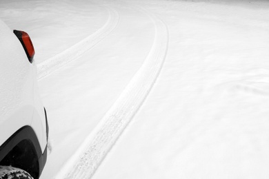 Modern car leaving tire tracks on snowy road, closeup view
