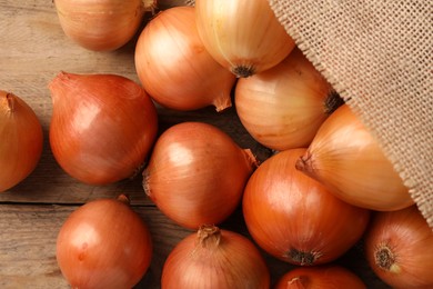 Many ripe onions on wooden table, flat lay