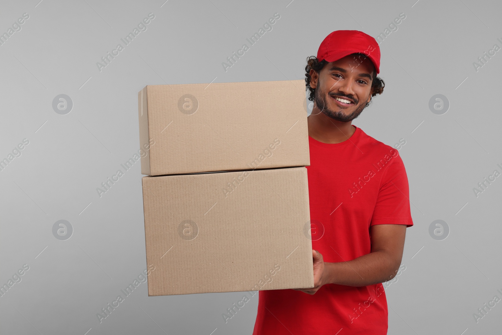 Photo of Happy young courier with parcels on grey background