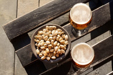 Glasses of cold beer and pistachios on wooden bench, flat lay