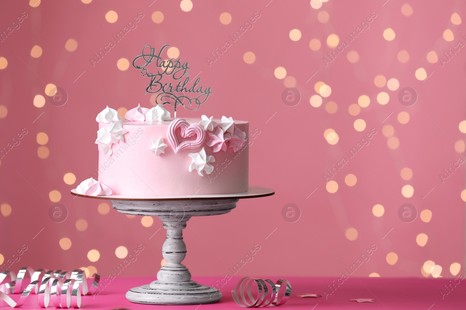 Photo of Beautifully decorated birthday cake on pink table against blurred festive lights, space for text