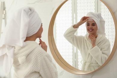 Photo of Beautiful young woman doing facial massage with gua sha tool in front of mirror at home