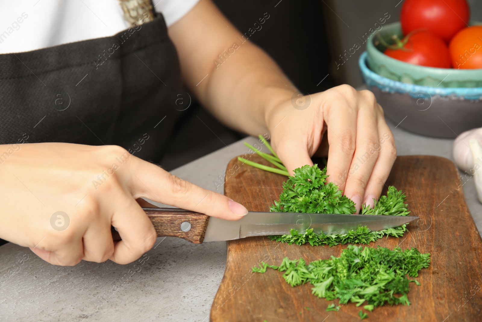 Photo of Woman cutting fresh green parsley on wooden board, closeup