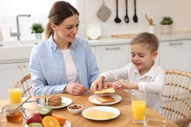 Mother and her cute little son having breakfast at table in kitchen