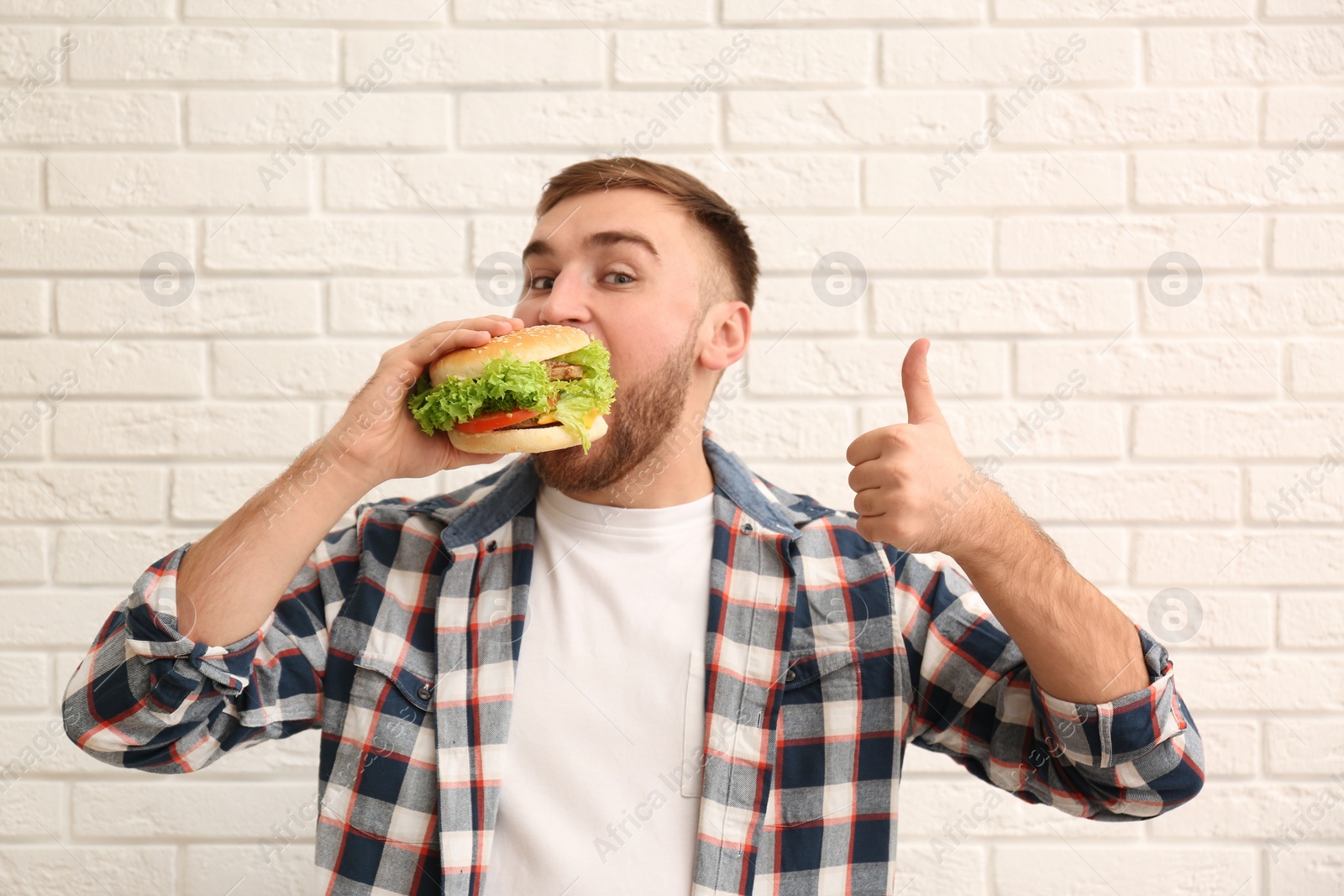 Photo of Young man eating tasty burger against brick wall