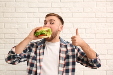 Young man eating tasty burger against brick wall